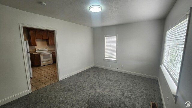 spare room with a textured ceiling, visible vents, light carpet, light tile patterned floors, and baseboards