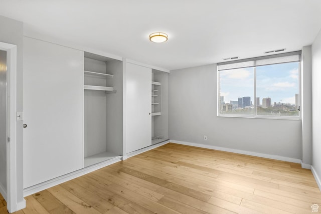 777 E S Temple S Unit 11B, Salt Lake City, UT 84102 - unfurnished bedroom featuring baseboards, hardwood / wood-style floors, visible vents, and a closet