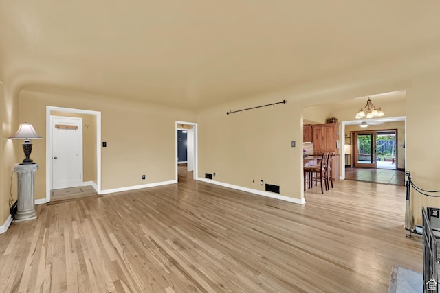 unfurnished living room with light wood finished floors, baseboards, and a chandelier