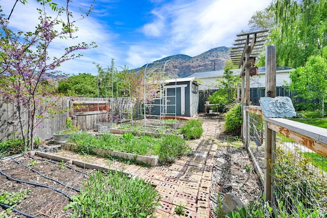fenced backyard with a vegetable garden, a storage shed, a mountain view, and an outbuilding