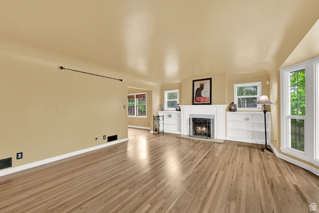 unfurnished living room featuring a lit fireplace, light wood finished floors, baseboards, plenty of natural light, and lofted ceiling