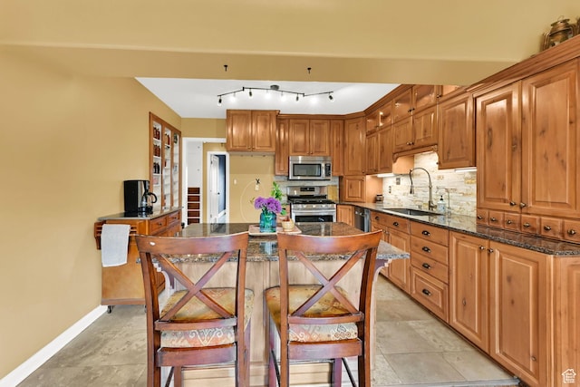 kitchen with appliances with stainless steel finishes, a sink, backsplash, baseboards, and dark stone countertops