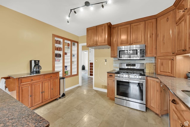 kitchen with stainless steel appliances, dark stone counters, baseboards, brown cabinets, and decorative backsplash