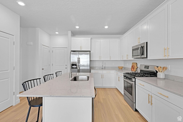 kitchen with a sink, light wood finished floors, a kitchen breakfast bar, and appliances with stainless steel finishes