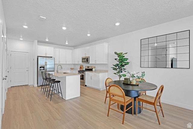 kitchen with a sink, a kitchen bar, light wood-style floors, white cabinets, and appliances with stainless steel finishes