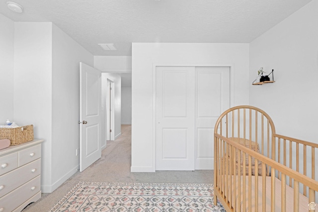 bedroom with a textured ceiling, a crib, a closet, and light colored carpet