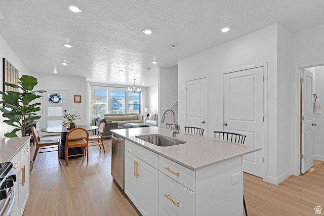 kitchen featuring light wood-style flooring, an island with sink, a sink, stainless steel appliances, and a chandelier