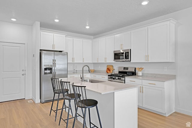 kitchen featuring appliances with stainless steel finishes, a sink, light wood-style floors, a breakfast bar area, and white cabinetry