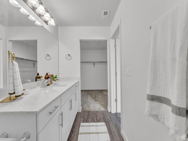 bathroom with a walk in closet, vanity, visible vents, and wood finished floors