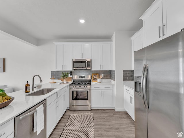 kitchen featuring a sink, stainless steel appliances, white cabinets, light wood-type flooring, and backsplash