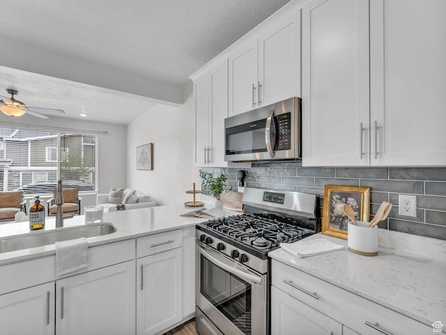 kitchen with a sink, stainless steel appliances, backsplash, open floor plan, and white cabinets