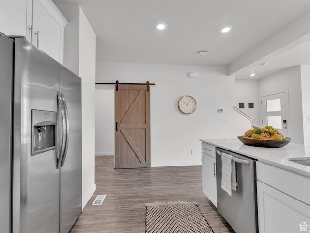 kitchen with a barn door, baseboards, visible vents, stainless steel appliances, and white cabinets