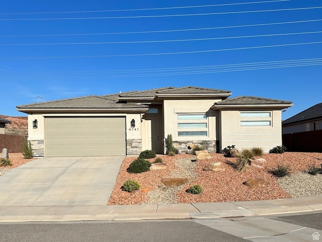 prairie-style house featuring concrete driveway, stone siding, stucco siding, and a garage