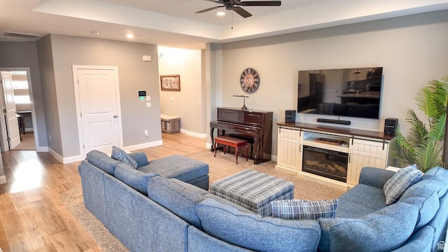 living room with a ceiling fan, recessed lighting, baseboards, a raised ceiling, and light wood-style floors