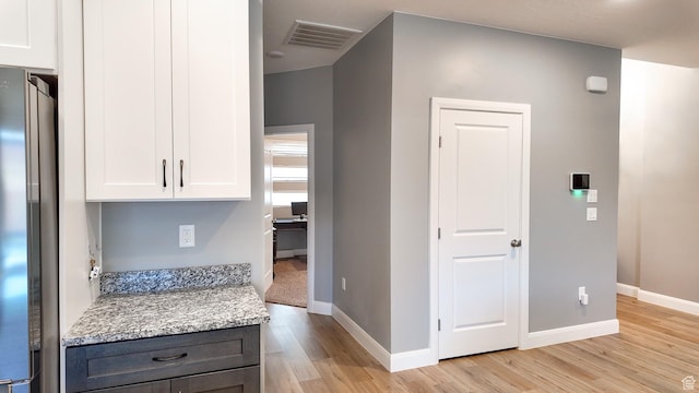 interior space with light wood finished floors, freestanding refrigerator, white cabinets, visible vents, and baseboards