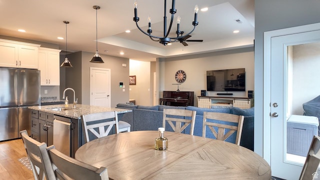 dining space with an inviting chandelier, light wood-type flooring, visible vents, a raised ceiling, and recessed lighting