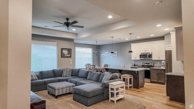 living room featuring a tray ceiling, light wood-type flooring, a ceiling fan, and recessed lighting