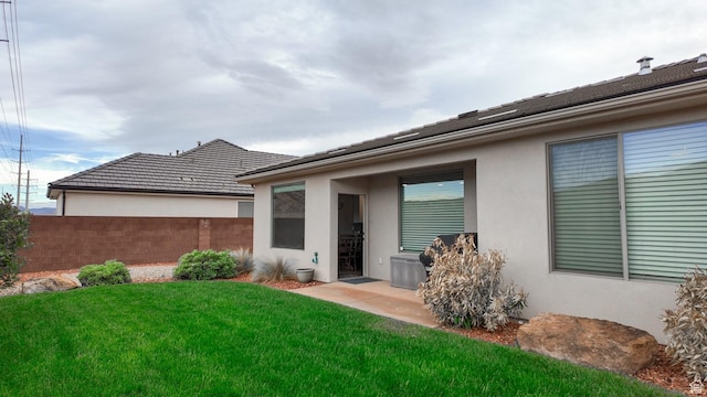 rear view of property featuring stucco siding, fence, and a lawn
