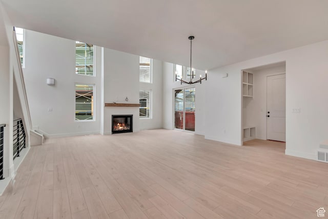 unfurnished living room featuring baseboards, a glass covered fireplace, visible vents, a chandelier, and light wood-type flooring