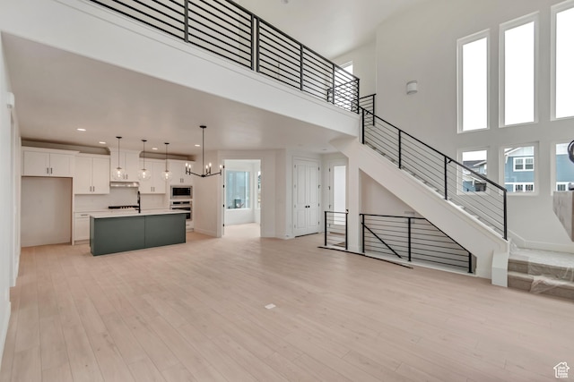 unfurnished living room featuring light wood finished floors, an inviting chandelier, stairway, and recessed lighting