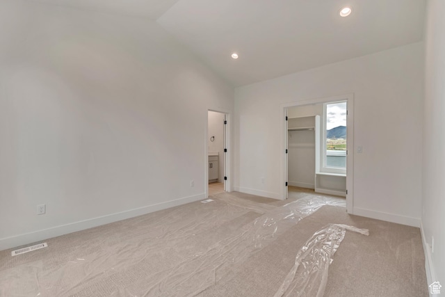 unfurnished bedroom featuring vaulted ceiling, light colored carpet, a walk in closet, and visible vents