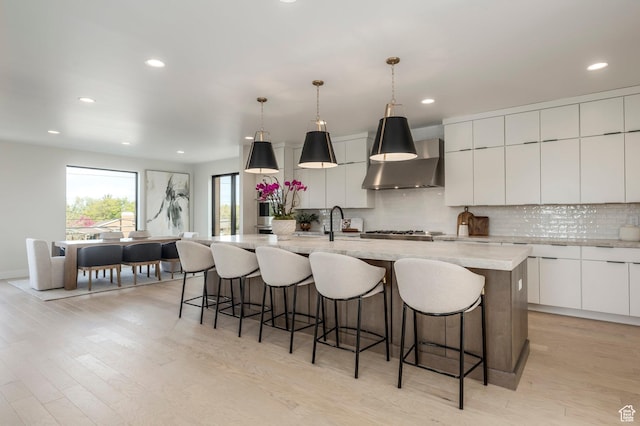 kitchen with wall chimney range hood, backsplash, modern cabinets, and light wood-style floors