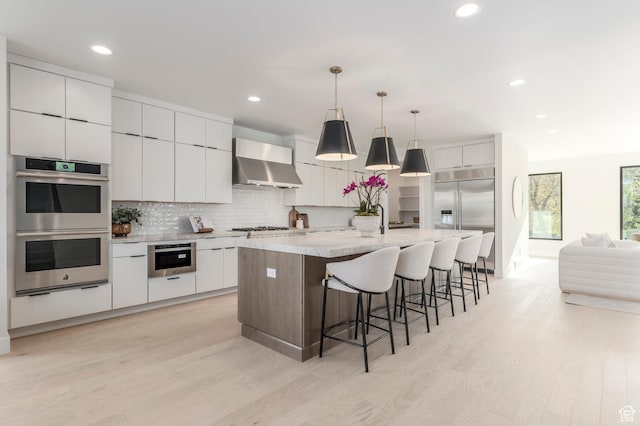 kitchen with light wood-style floors, backsplash, wall chimney range hood, appliances with stainless steel finishes, and recessed lighting