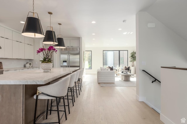 kitchen with light wood-style flooring, stainless steel built in refrigerator, a breakfast bar, modern cabinets, and light countertops
