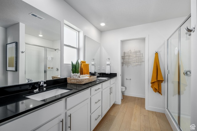 bathroom with a sink, toilet, visible vents, a stall shower, and wood-type flooring
