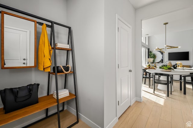 corridor with baseboards, a notable chandelier, and light wood-style floors