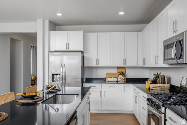 kitchen with a sink, dark countertops, white cabinets, light wood-type flooring, and appliances with stainless steel finishes