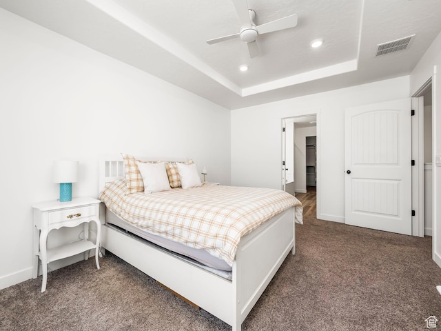 carpeted bedroom featuring a tray ceiling, recessed lighting, baseboards, ceiling fan, and visible vents