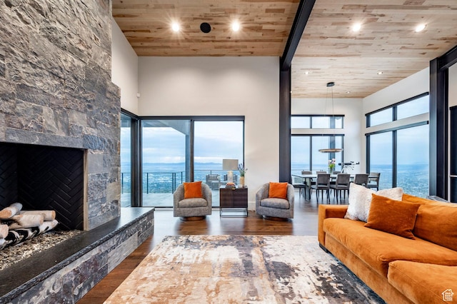 living room with wooden ceiling, wood finished floors, a high ceiling, recessed lighting, and a stone fireplace