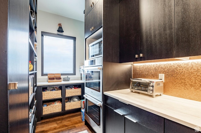 kitchen featuring stainless steel appliances, a toaster, dark wood-style flooring, backsplash, and light countertops