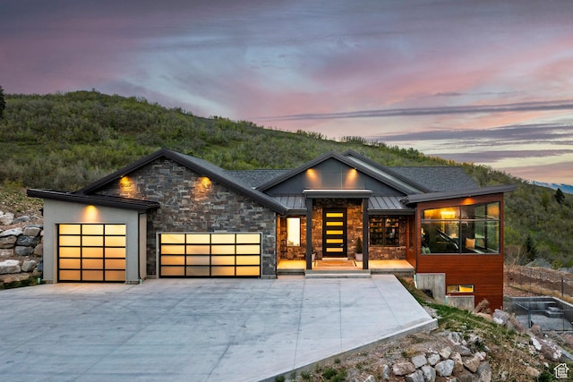 modern home featuring stone siding, a garage, metal roof, driveway, and a standing seam roof