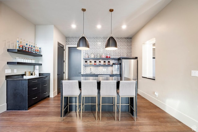 kitchen featuring open shelves, dark cabinetry, a kitchen bar, backsplash, and recessed lighting