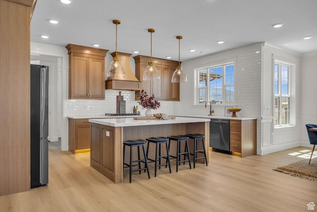 kitchen featuring custom range hood, a kitchen breakfast bar, light wood-style floors, light countertops, and appliances with stainless steel finishes