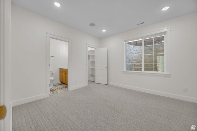 unfurnished bedroom featuring visible vents, recessed lighting, light carpet, a walk in closet, and baseboards