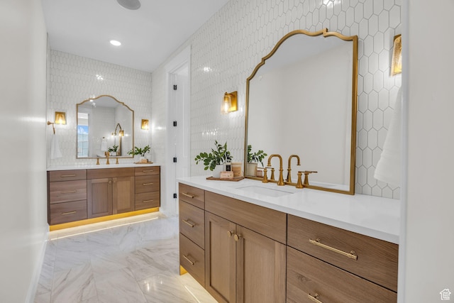bathroom featuring wallpapered walls, marble finish floor, two vanities, and a sink