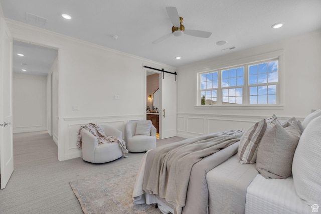 bedroom featuring a decorative wall, a barn door, visible vents, recessed lighting, and crown molding
