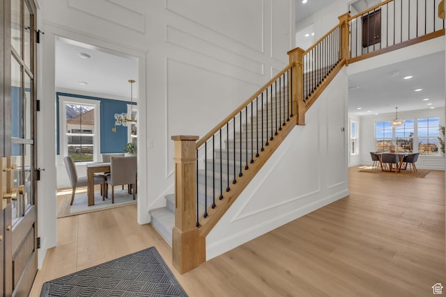 staircase with a wealth of natural light, wood finished floors, a decorative wall, and a notable chandelier