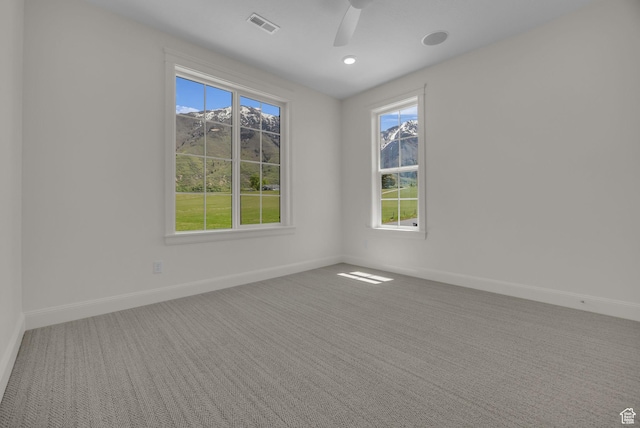 carpeted spare room with ceiling fan, a wealth of natural light, baseboards, and visible vents