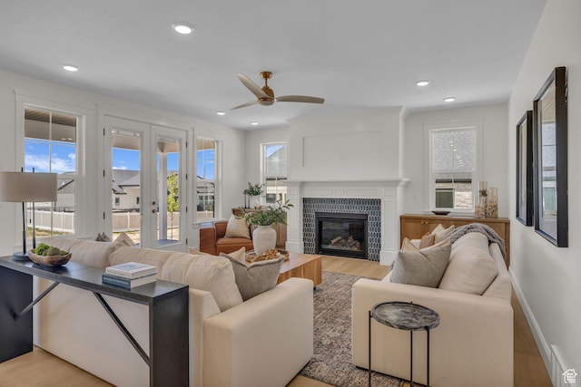 living room with a tile fireplace, light wood-type flooring, french doors, and ceiling fan