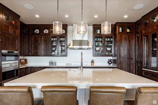 787 N Red Ledges Blvd, Heber City, UT 84032 - kitchen with wall chimney range hood, decorative light fixtures, a breakfast bar area, an island with sink, and dark brown cabinetry