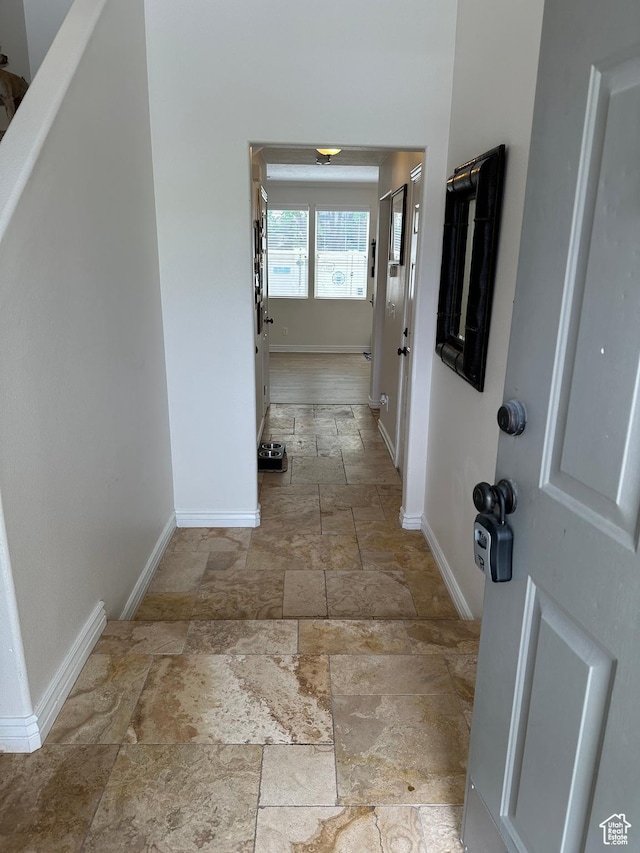 hall featuring baseboards and stone tile flooring