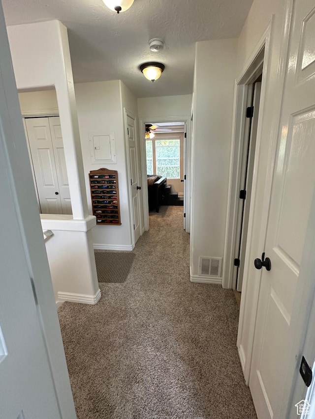 corridor featuring a textured ceiling, carpet flooring, baseboards, and visible vents