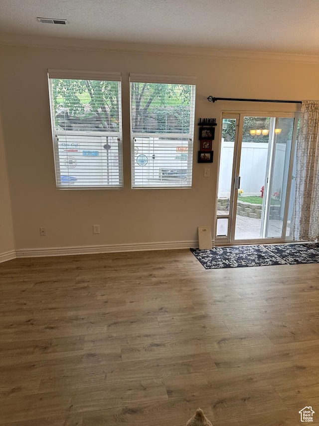 empty room with crown molding, wood finished floors, and baseboards