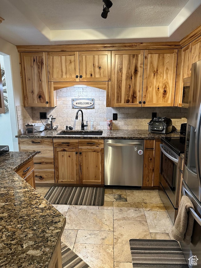 kitchen featuring stone finish floor, brown cabinetry, a sink, stainless steel appliances, and tasteful backsplash