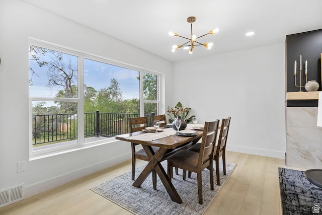 dining space featuring light wood-type flooring, a notable chandelier, visible vents, and baseboards