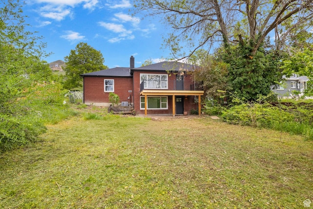 back of property featuring a lawn, brick siding, a chimney, and a deck